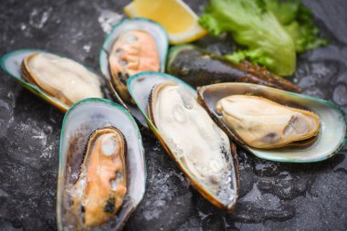 Deniz ürünleri midye buğulama / siyah tabakta taze midye ve limon ve marul ile pişirilmiş yiyecek.