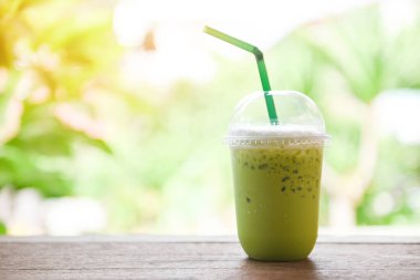 Yeşil çay smoothie / Matcha yeşil çay. Plastik bardakta süt ve ahşap masa ve doğa yeşili arka plan.