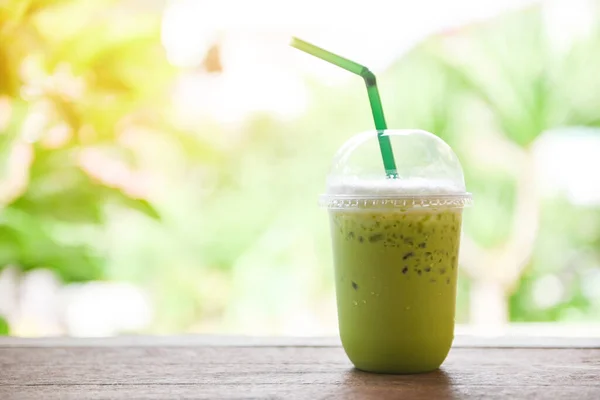 Green tea smoothie / Matcha green tea with milk on plastic glass on the wooden table and nature green background