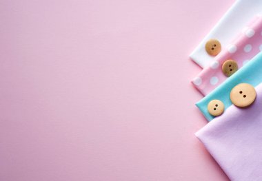 Farklı renklerde pamuk kumaş ve pembe arka planda puantiyeli saten kurdeleler. Metin için boşluk, üst görünüm