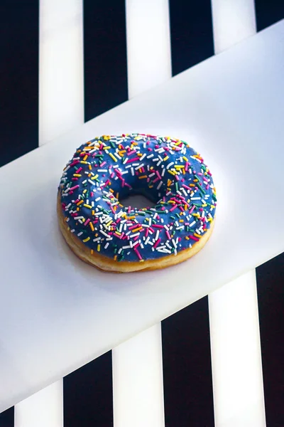 Rosquilla dulce con hielo y polvo de color, sobre un fondo blanco con rayas blancas y negras en los lados, vista superior . — Foto de Stock