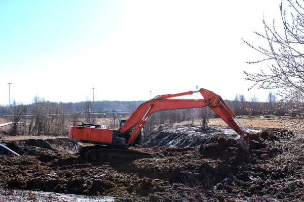 Строительная техника выкапывает яму. оранжевый экскаватор работает в грунте. Весна, солнечный день . — стоковое фото
