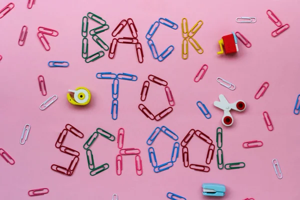 Gekleurde paperclips op een roze achtergrond bekleed met de inscriptie-terug naar school. — Stockfoto
