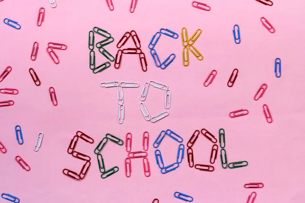 Kolorowe spinki do papieru na różowym tle pokryte napisem-powrót do szkoły. — Zdjęcie stockowe