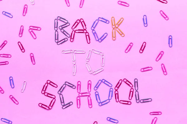 Colored paper clips on a pink background lined with the inscription - back to school. — Stock Photo, Image