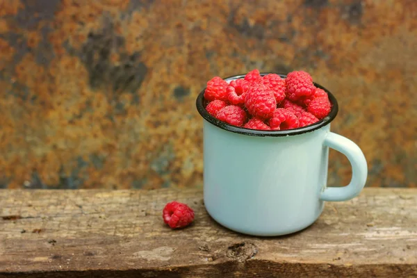 La tasse vintage en métal bleu est pleine de framboises. collation juteuse, savoureuse et saine. récolte . — Photo