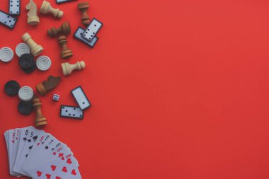 Kırmızı arka planda masa oyunları: iskambil kağıtları, domino taşları, dama ve satranç