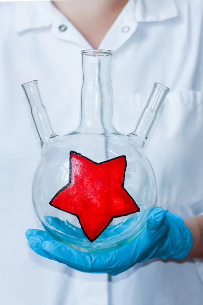 La mano del guante de los químicos sostiene un matraz de tres gargantas para un ambiente festivo. las vacaciones en el trabajo . — Foto de Stock