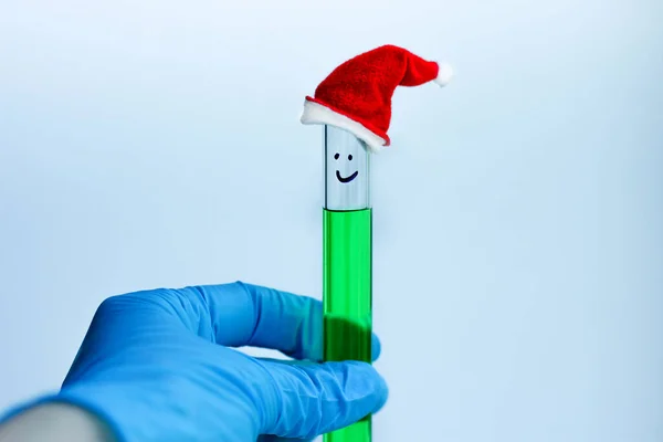 a blue-gloved hand holds a test tube with a green solution with a decorative red cap in the chemical laboratory
