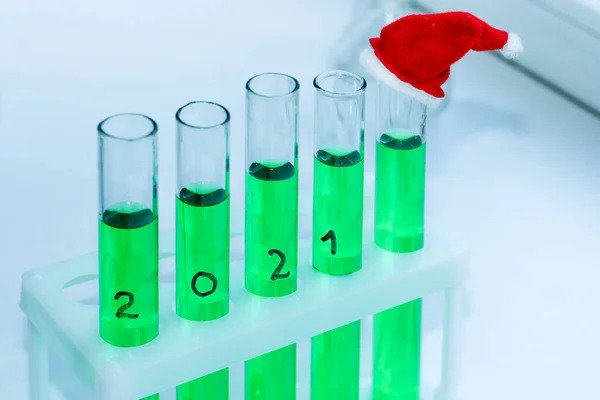 five vials of green solution in a chemical lab. on the end tube is a miniature decorative red cap. new year mood at work