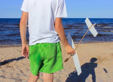 Bir gölün ya da denizin kıyısında ev yapımı uçağı olan bir çocuk kalkışa hazırlanıyor..