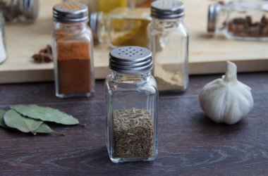 koyu ahşap arka plan üzerinde bir ışık kesme tahtası üzerinde baharatlar ile cam kavanozlar