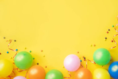 Renkli balon, konfeti ve sarı tablo üst görünümünde şekerler yığını. Doğum günü partisi arka plan. Bayram tebrik kartı.