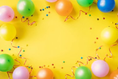 Renkli balon, konfeti ve sarı tablo üst görünümünde şekerler yığını. Doğum günü partisi arka plan. Bayram tebrik kartı.