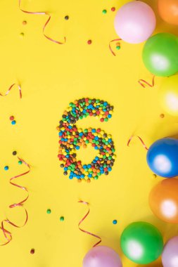 Sarı arka plan üzerinde renkli balonlar ile 6 numaralı şekerler. Doğum günü için kavram.