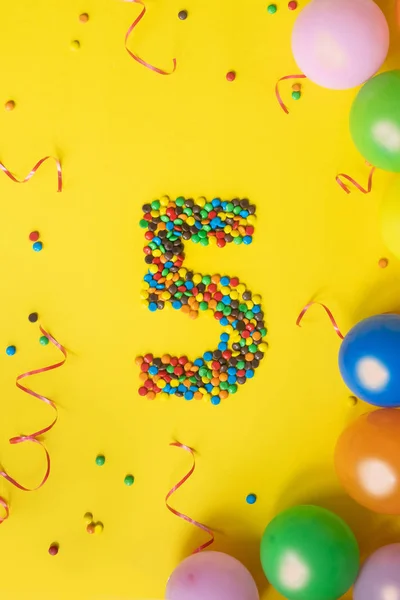 Happy Birthday number 5 made of candies with colorful balloons on yellow background.