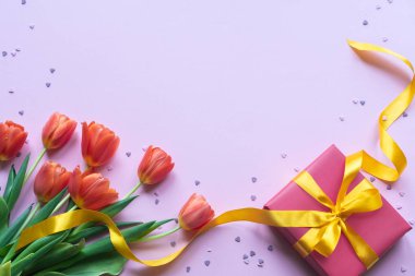 Red tulips and gift box with yellow ribbon on pink background. Copy space.