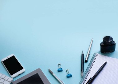 İş düz yatıyordu: dizüstü bilgisayar, kalem, telefon, mavi arka plan üzerinde gözlük ile masa. Kopyalama alanı