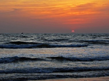 Güzel günbatımının arka planında dalgalarla denizde seyreden küçük bir tekne..