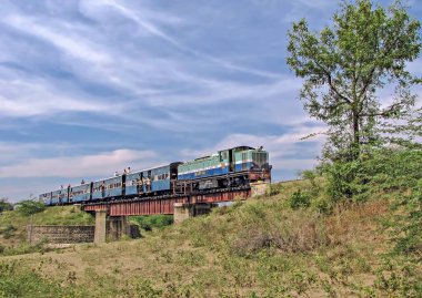 Shindawane, Pune, Hindistan: 16 Ocak 2016 - Uzun bir tren mavi gökyüzünün açık bir zemininde bulutlu bir tünelden çıkıyor.