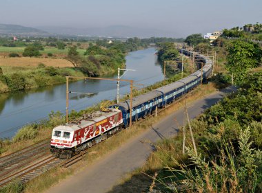 Shindawane, Pune, Hindistan: 16 Ocak 2016 - Uzun bir tren mavi gökyüzünün açık bir zemininde bulutlu bir tünelden çıkıyor.