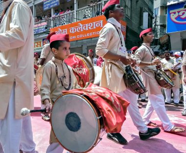 Pune, Maharashtra, Hindistan-22 Eylül 2010: Kırmızı şapkalı, büyük çocukları olan küçük çocuk, Ganesh festival alayında geleneksel dhol 'u yeniyor.