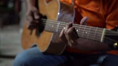 Gitarist dinlenme zamanında akustik gitar çalıyor, adamın parmağı bar akorunu tutuyor.