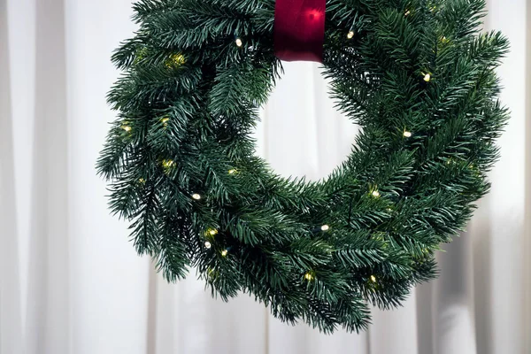 Christmas fir-tree wreath with red tape illuminated by garland