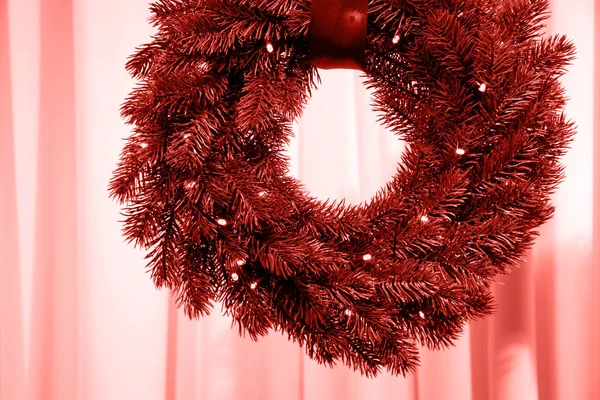 Christmas fir-tree wreath with tape illuminated by garland in colour of Living Coral