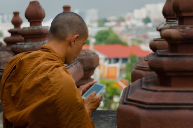 Buddhist monk looking at the smart phone on the top of the temple in Bangkok clipart