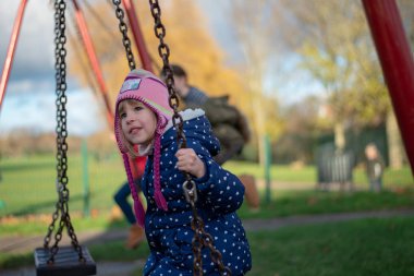 Salıncak üzerinde oyun alanında okul öncesi yaşında beyaz kadın arka hızıyla tarafsız bakmak gülümseyen.