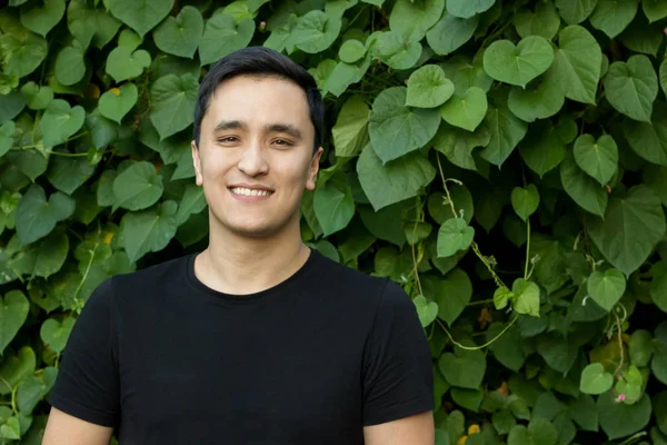 Asian young man in black t-shirt on beautiful green plant background , healthy lifestyle.