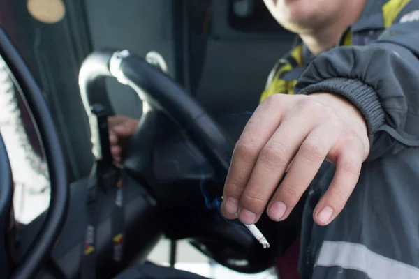 Truck or bus driver hands holding steering wheel and smoking cigarette in public places.