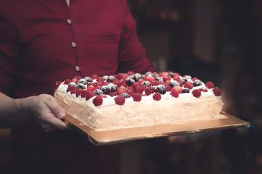 Kırmızı gömlekli bir adam elinde bir kafede karanlık bir arka plan üzerinde berry pie taşır