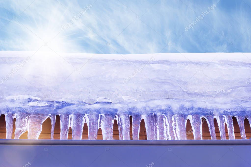 Icicles hanging on the roof of a wooden building under the bright sunrays of spring. Nice warm weather. There is a blue sky at the top of the frame.