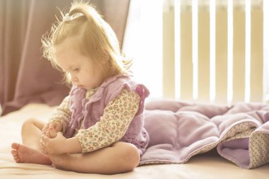 Bir yatak Toddler kız sabah güneşte onu küçük ayaklar bakıyor üzerinde oturan kirişler