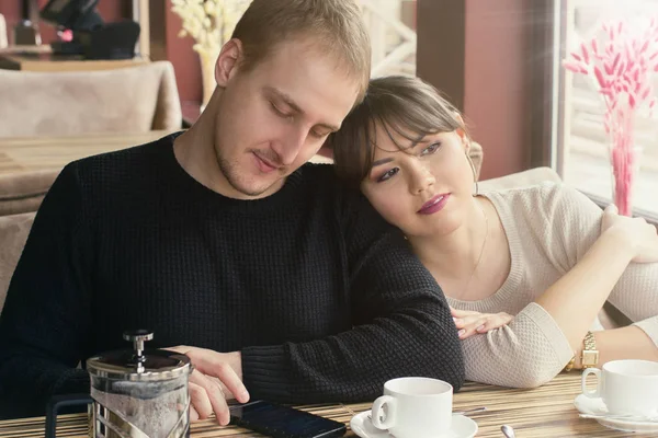 Een jonge Aziatische vrouw en Kaukasische man paar zitten in Cafe. Haar hoofd is liggend op de schouder van het kijken op een smartphone-man. — Stockfoto