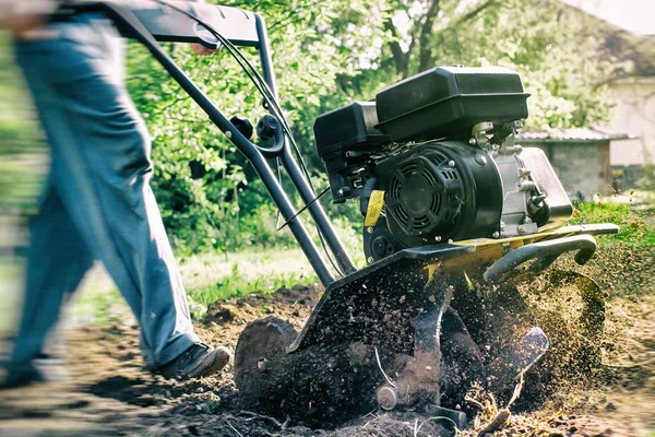 Ein Mann pflügt einen Boden mit einem Motormulch bei Gartenarbeiten im Freien — Stockfoto