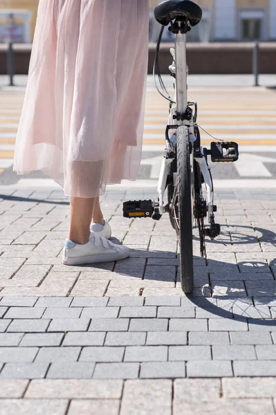 Pernas de mulher em pé perto de bicicleta e pernas de homem na bicicleta na frente da estrada transversal — Fotografia de Stock