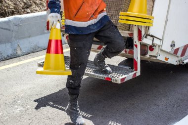 Trafik hattı boyama. İşçiler dağ yolunda beyaz sokak çizgisi çiziyorlar. Arka planda kırmızı ve sarı çizgili, yol yapım çalışmaları sırasında asfalt üzerinde duran yol konileri