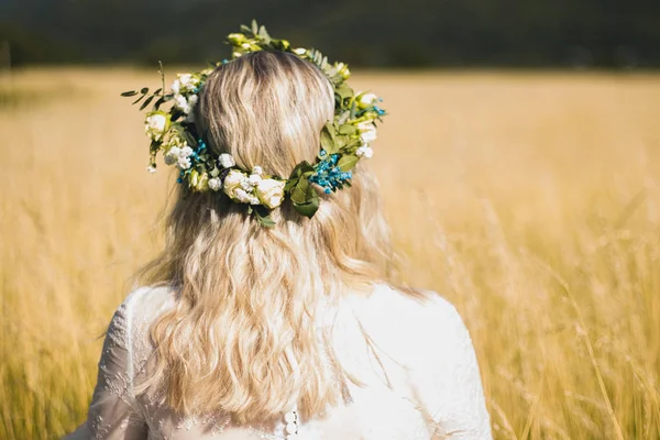 Boho tarzında beyaz elbiseli genç kadının arkası, yazın tarlada çiçekçe çelengi ile.