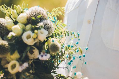 Damat gelin buketi tutar. Yakın çekim, yumuşak odaklama, dış mekan.
