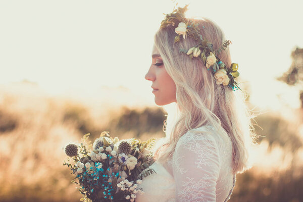 Beautiful young woman portrait in a white dress in boho style with a floral wreath in the summer in the field. Selective soft focus.