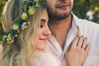 Güneşli yaz gününde beyaz elbiseli gelin ve çelenk ve damat portresi. Rustik açık düğün konsepti. Yumuşak seçici odaklama.