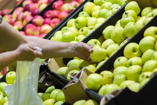 Alte Frau wählt frische Äpfel in Lebensmittelgeschäft produzieren Abteilung und legt sie in Plastiktüte. — Stockfoto