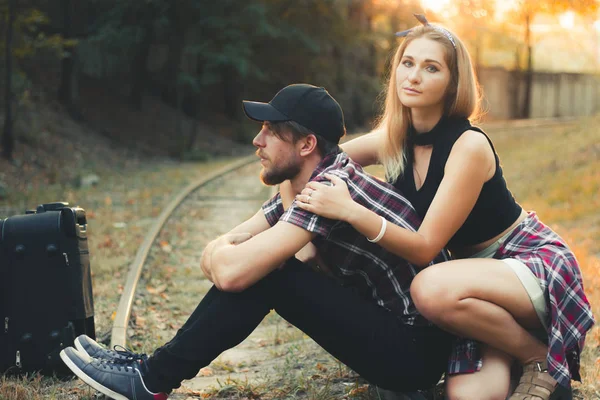 電車の中でスーツケースを着た若いカップル。恋人たちはレールの上で列車を待っている。秋の日没時に列車に遅れ絶望的な旅行者。. — ストック写真