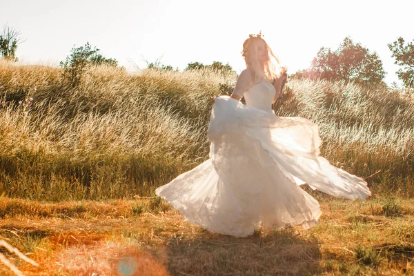 Gelin beyaz gelinlik haddeleme ve gün batımı ışığında dans bir yaz alanında. Şeffaf elbise etek kumaşı ile görülen güneş Kirişleri. Rustik veya boho açık düğün konsepti. Seçici yumuşak odaklama. — Stok fotoğraf