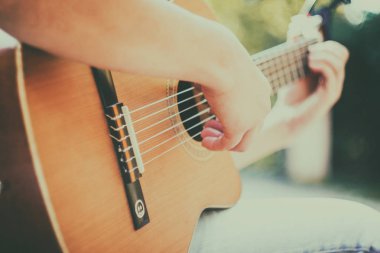 Capo 'nun parktaki gitar boynunu kapat. Parktaki bankta oturan genç adam gitar çalıyor. Genç ve çekici bir adam son bahar tatilinde güneşli günlerde canlı müzik dinlemekten hoşlanıyor. Kullanılan Retro lens.