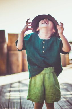 Kırsal kesimde, kahverengi şapkalı ve çarşaf giymiş, yaz günü giyimli mutlu, duygusal küçük bir kızın portresi..