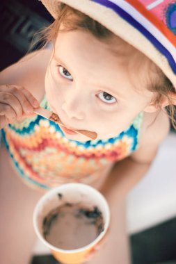Örgü mayolu, şapkalı, kağıt bardaktan erimiş dondurma yiyen küçük tatlı bir kızın portresi..